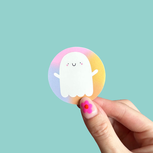 A hand holding a cute ghost sticker on a gradient colourful background - Nutmeg and Arlo