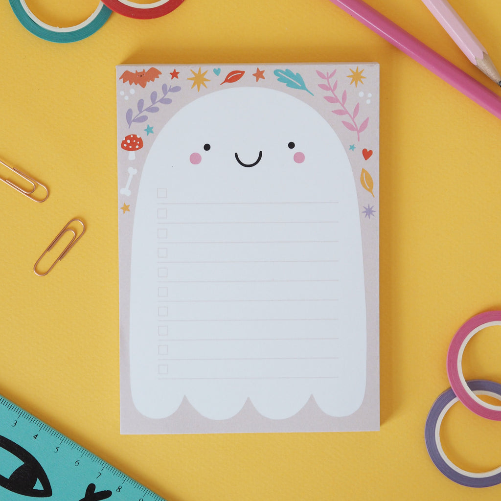 A cute ghost notepad on a yellow background with random stationery items around the outside for decoration - Nutmeg and Arlo