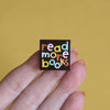 a hand holding an enamel pin with the words 'read more books' - nutmeg and arlo