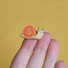 a hand holding a snail enamel pin - nutmeg and arlo