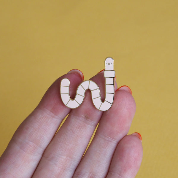 a hand holding a worm enamel pin - nutmeg and arlo