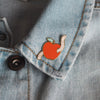 an enamel pin of an apple with a worm in it on a denim jacket - nutmeg and arlo